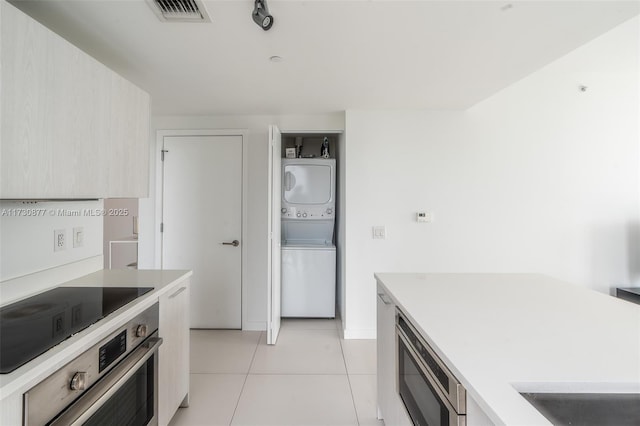 kitchen with light tile patterned floors, oven, and stacked washer / dryer