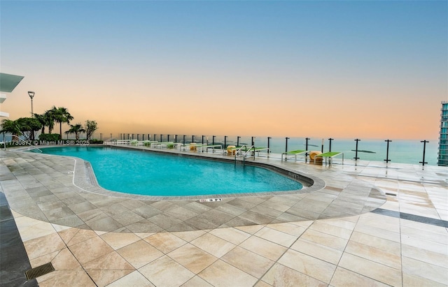 pool at dusk with a water view and a patio area