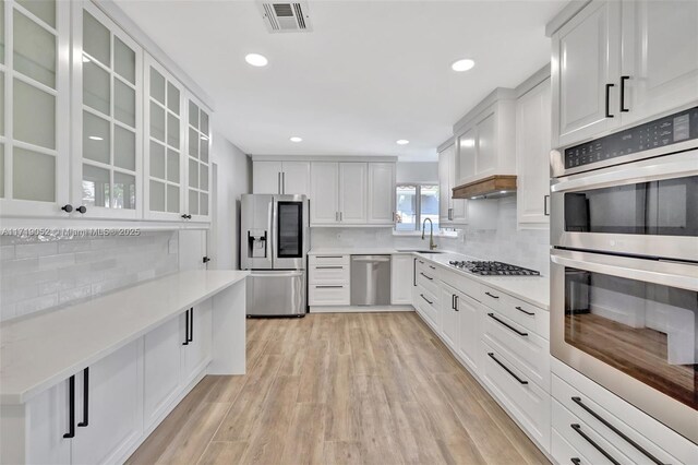 kitchen featuring white cabinetry, decorative backsplash, light hardwood / wood-style floors, and appliances with stainless steel finishes