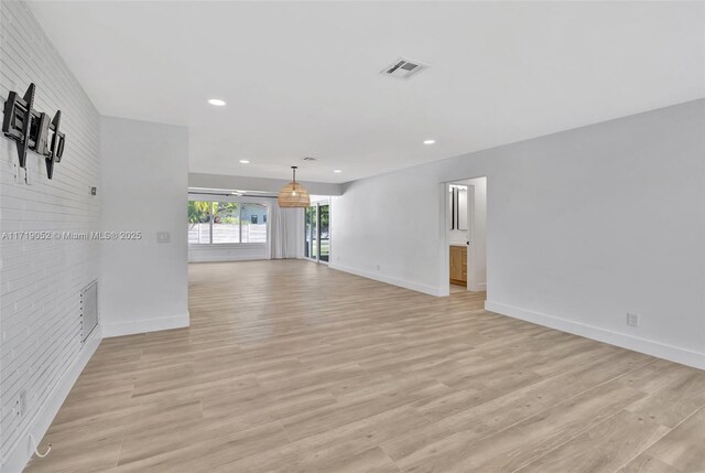 unfurnished living room featuring brick wall and light hardwood / wood-style flooring