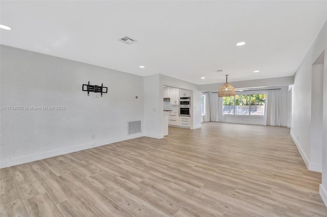 unfurnished living room with brick wall and light hardwood / wood-style flooring