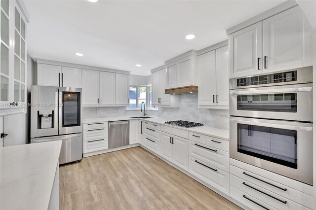 kitchen featuring light stone counters, light wood-type flooring, white cabinets, stainless steel appliances, and backsplash