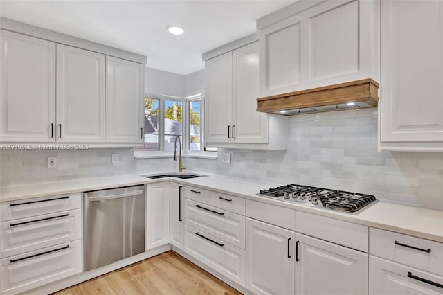 kitchen with sink, stainless steel appliances, custom range hood, white cabinets, and light wood-type flooring