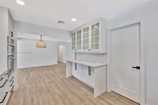 kitchen featuring pendant lighting, double oven, white cabinets, decorative backsplash, and light wood-type flooring