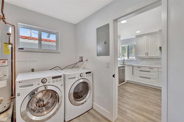 laundry area with sink, light wood-type flooring, electric panel, washing machine and dryer, and water heater