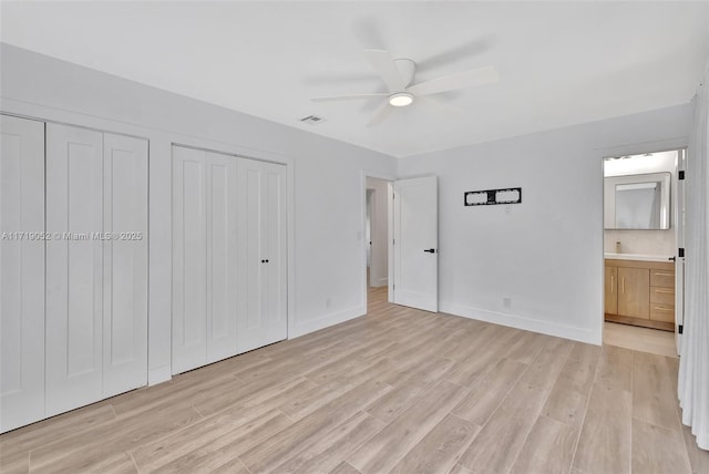 unfurnished bedroom with ceiling fan, ensuite bath, multiple closets, and light wood-type flooring