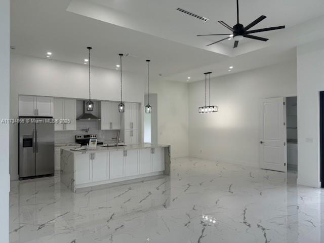 kitchen with stainless steel appliances, an island with sink, decorative light fixtures, and wall chimney exhaust hood