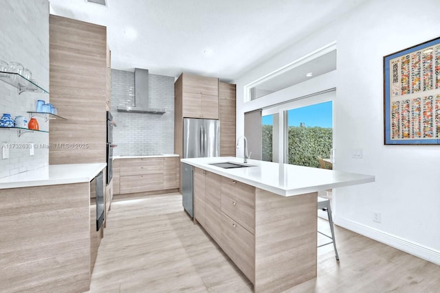 kitchen with sink, a breakfast bar area, stainless steel appliances, a kitchen island with sink, and wall chimney range hood