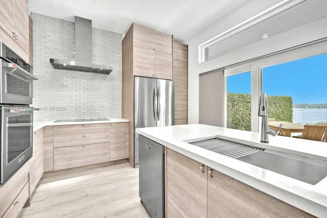 kitchen with appliances with stainless steel finishes, sink, light brown cabinets, a textured ceiling, and wall chimney exhaust hood