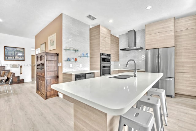 kitchen with appliances with stainless steel finishes, a breakfast bar, a center island with sink, and wall chimney exhaust hood