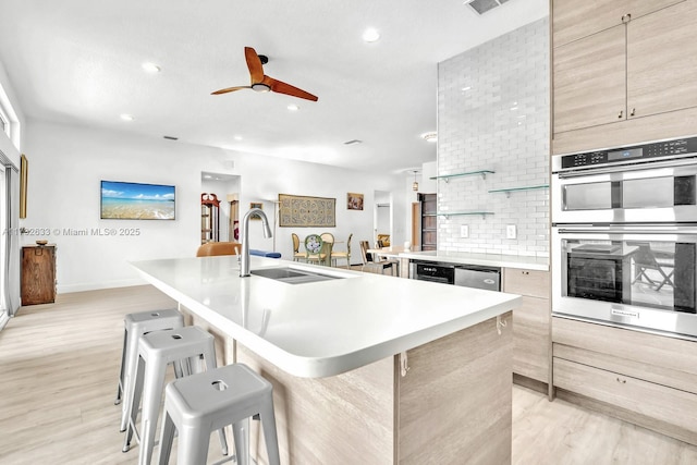 kitchen featuring double oven, sink, an island with sink, and a kitchen bar