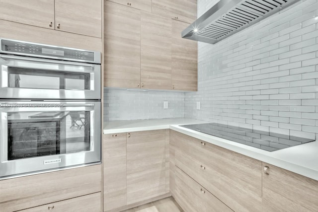 kitchen with wall chimney exhaust hood, light brown cabinetry, double oven, and decorative backsplash