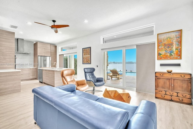 living room featuring a water view, sink, ceiling fan, and light hardwood / wood-style flooring