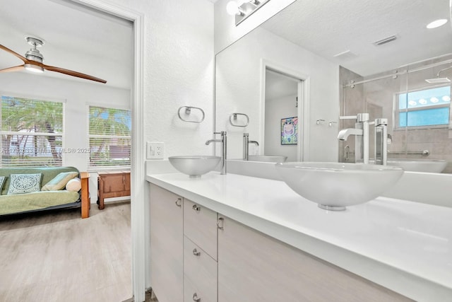 bathroom featuring wood-type flooring, vanity, ceiling fan, walk in shower, and a textured ceiling