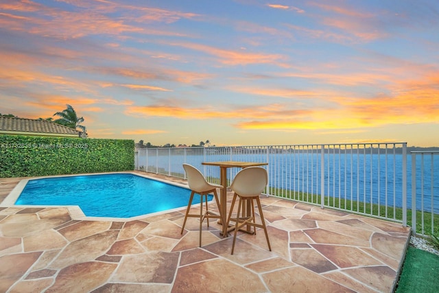 pool at dusk featuring a patio area and a water view