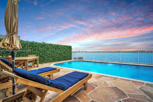 pool at dusk with a patio area and a water view