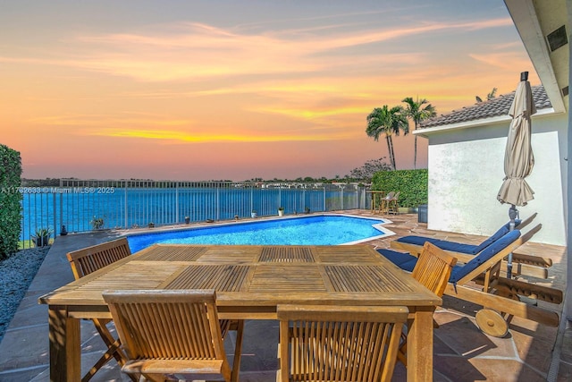 pool at dusk featuring a water view and a patio area