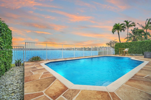 pool at dusk featuring a patio and a water view