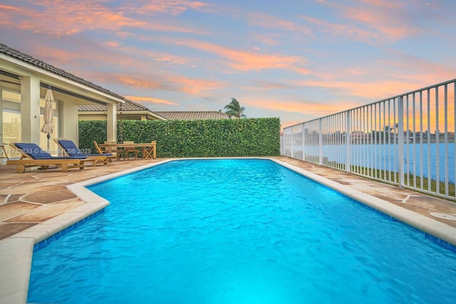 pool at dusk with a water view and a patio area