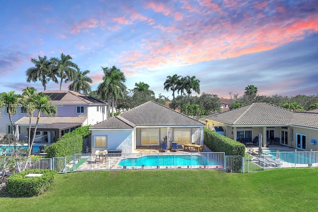 pool at dusk with a patio area and a lawn