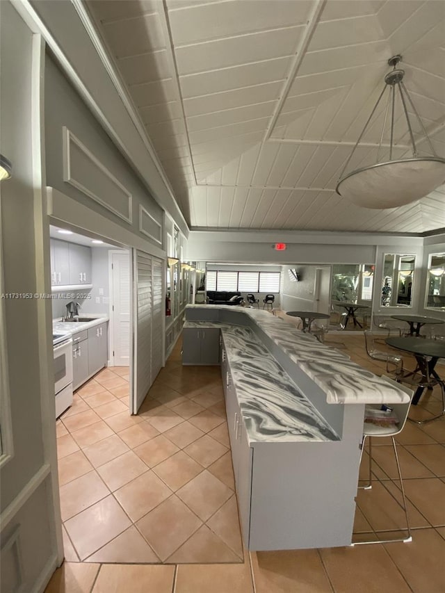 kitchen featuring hanging light fixtures, light stone countertops, white cabinets, light tile patterned flooring, and white electric stove