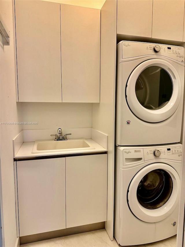 laundry area featuring sink, cabinets, and stacked washer / dryer