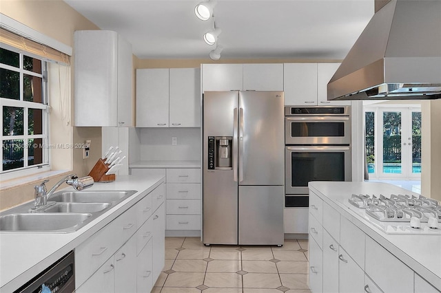 kitchen with appliances with stainless steel finishes, island range hood, white cabinetry, sink, and track lighting