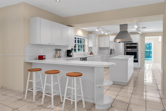 kitchen with appliances with stainless steel finishes, a kitchen breakfast bar, kitchen peninsula, island exhaust hood, and white cabinets