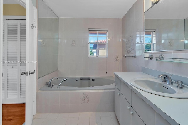 bathroom featuring a relaxing tiled tub, tile patterned floors, vanity, and tile walls