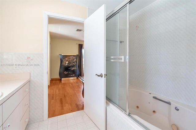 bathroom featuring vanity, shower / bath combination with glass door, tile patterned flooring, and tile walls