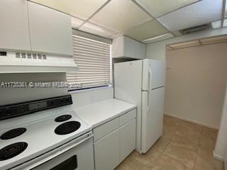 kitchen featuring light tile patterned flooring, ventilation hood, white cabinets, a drop ceiling, and white appliances