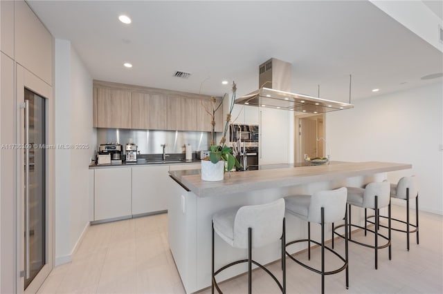 kitchen with a kitchen island, sink, island range hood, and light brown cabinetry