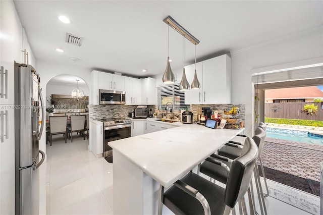 kitchen featuring decorative light fixtures, appliances with stainless steel finishes, a kitchen breakfast bar, kitchen peninsula, and white cabinets