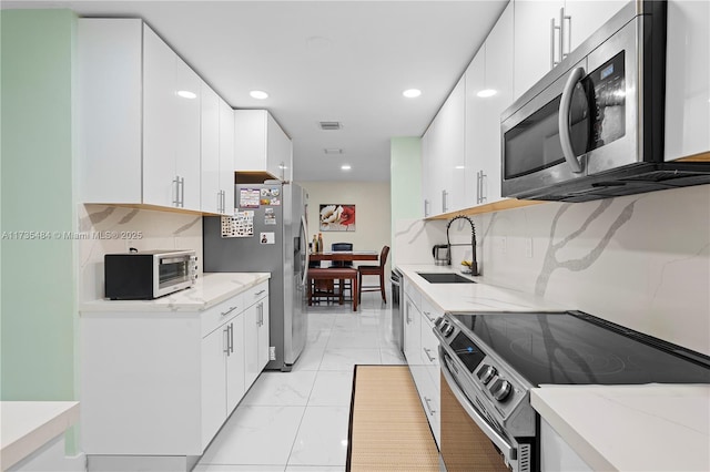 kitchen featuring appliances with stainless steel finishes, sink, white cabinets, decorative backsplash, and light stone countertops