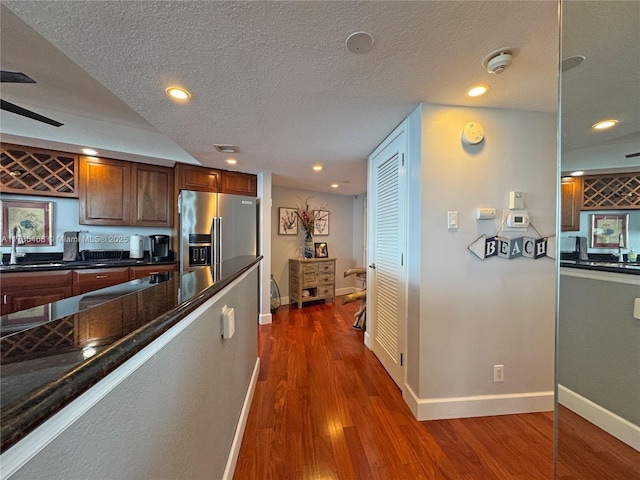 kitchen with a textured ceiling, baseboards, dark wood-type flooring, and stainless steel fridge with ice dispenser