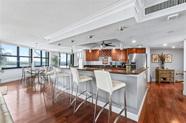 kitchen with visible vents, brown cabinetry, stainless steel fridge with ice dispenser, dark countertops, and a kitchen breakfast bar