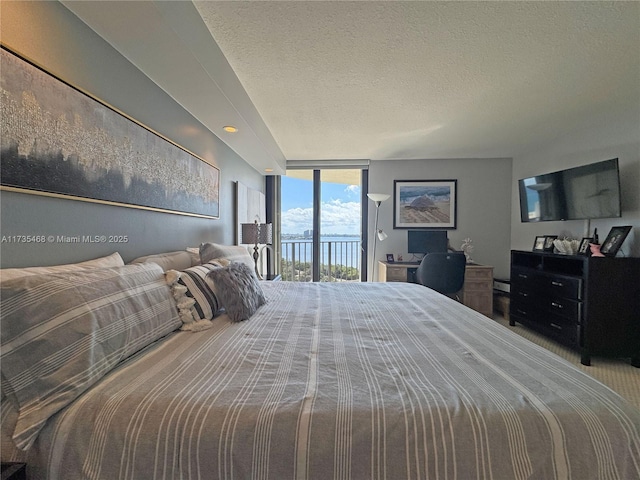 bedroom with access to outside, a wall of windows, and a textured ceiling