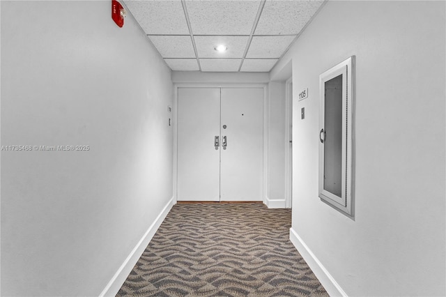 corridor featuring a paneled ceiling, carpet flooring, and baseboards