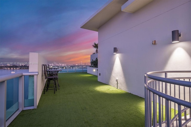 yard at dusk featuring a water view and a balcony