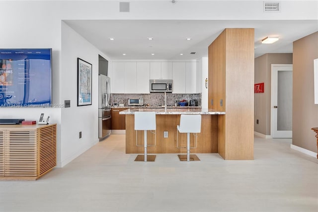 kitchen with visible vents, modern cabinets, light stone counters, stainless steel appliances, and decorative backsplash