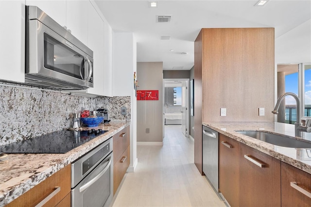 kitchen featuring a sink, light stone counters, appliances with stainless steel finishes, brown cabinetry, and decorative backsplash