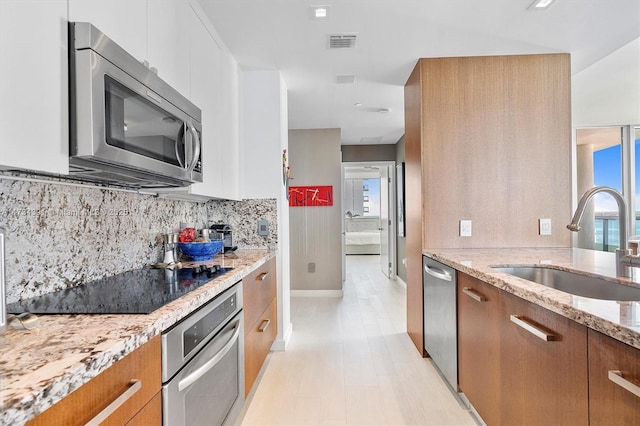 kitchen with visible vents, light stone counters, brown cabinetry, stainless steel appliances, and a sink