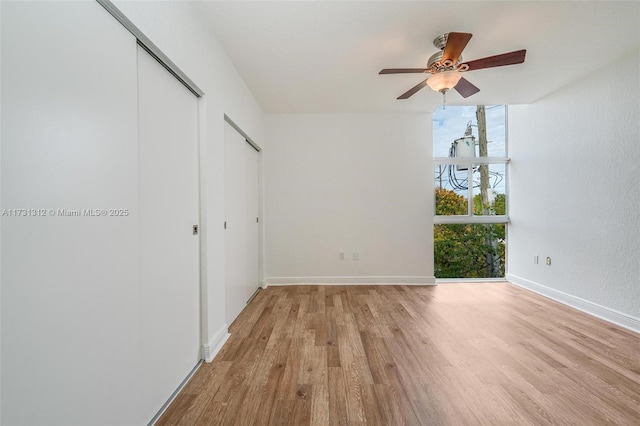 unfurnished bedroom with expansive windows, multiple closets, ceiling fan, and light hardwood / wood-style flooring