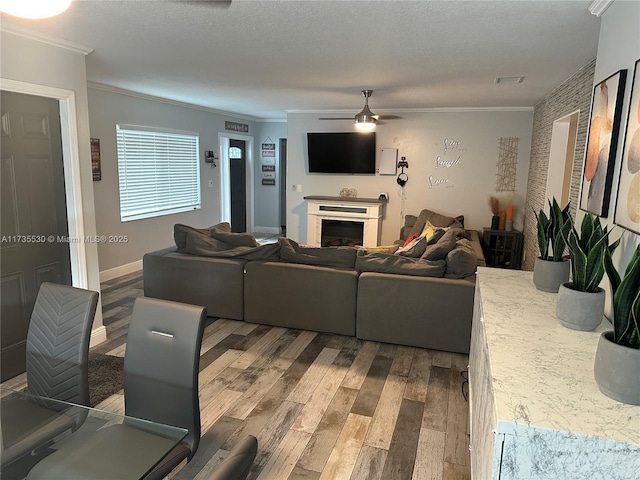 living room featuring ceiling fan, ornamental molding, wood-type flooring, and a textured ceiling