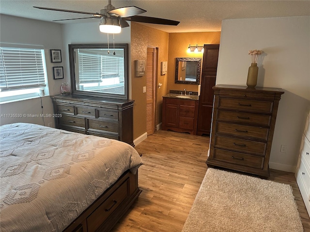 bedroom featuring connected bathroom, sink, ceiling fan, light hardwood / wood-style floors, and a textured ceiling