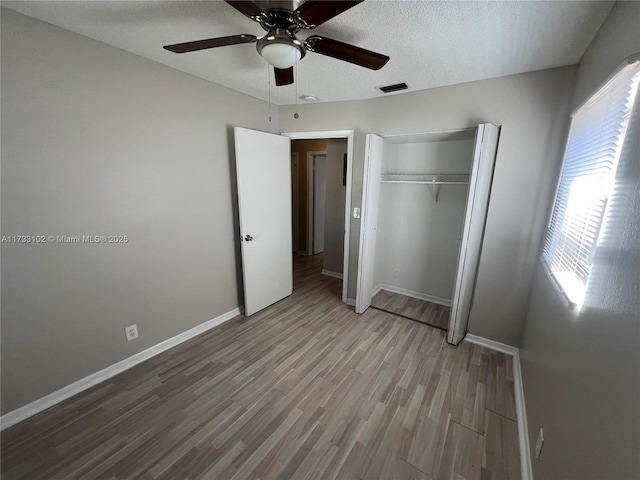 unfurnished bedroom with ceiling fan, hardwood / wood-style floors, a closet, and a textured ceiling