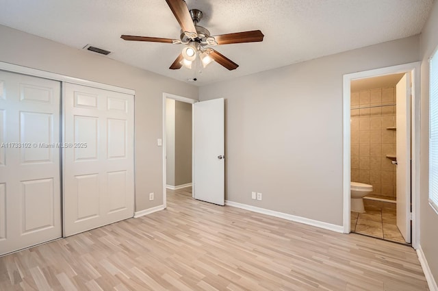 unfurnished bedroom featuring light hardwood / wood-style flooring, a closet, a textured ceiling, and ensuite bathroom