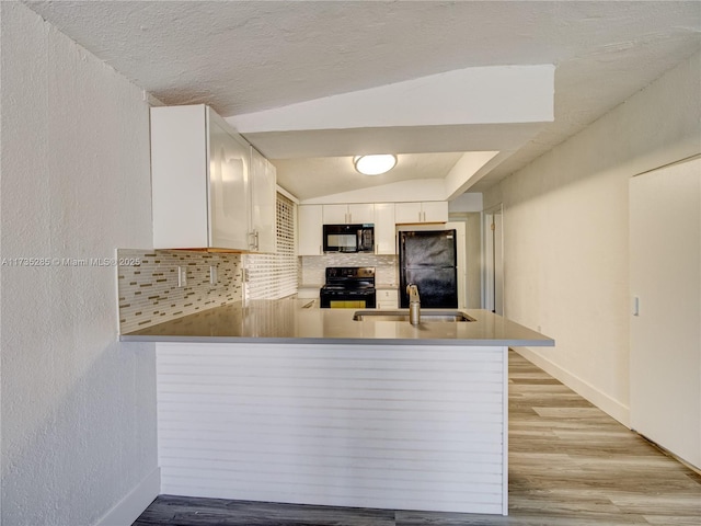 kitchen with white cabinetry, vaulted ceiling, kitchen peninsula, and black appliances