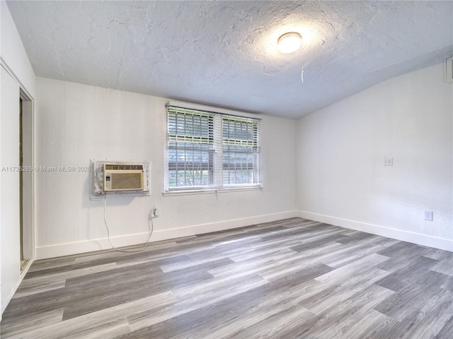 unfurnished room featuring hardwood / wood-style flooring, a wall mounted AC, and a textured ceiling