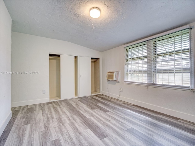 unfurnished bedroom featuring lofted ceiling, a wall mounted air conditioner, light hardwood / wood-style flooring, a textured ceiling, and a closet